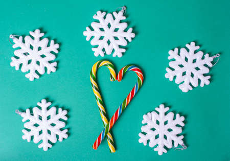 Heart shape with Christmas candy canes, white large snowflakes on a green background, top view. Can be used as a postcard or background for Christmas and New Years, Valentine's Dayの写真素材