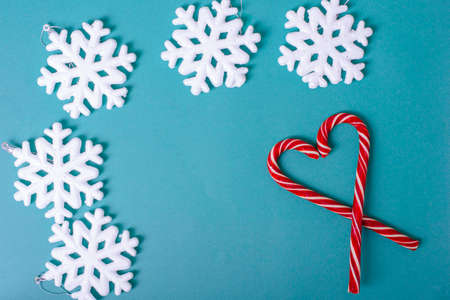 Heart shape with red Christmas candy canes, white large snowflakes, silvery balls on a blue background, top view.の写真素材