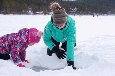 Two girls sculpt from snow, girls push snow aside to look at frozen ice, winter games outside, copy...