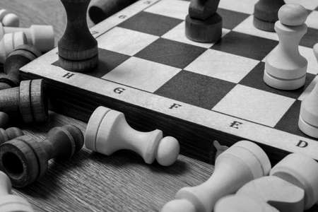 End of the chess game, chess pieces lie near the chessboard on the table, top view, black and white