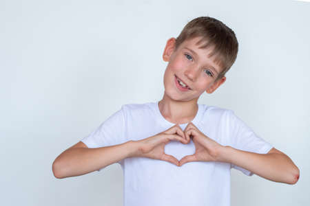 Portrait of a smiling boy making a heart, putting his hands on a heart on a white background, copy spaceの写真素材