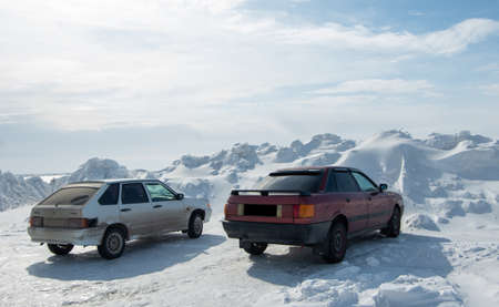 Rear view of cars standing by a huge snowdrift formed after clearing the roads from snow. High...