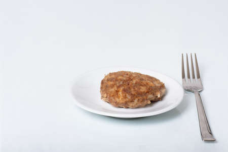Cooked meat patty on a white plate next to a fork isolated on white background, close-up, copy space. Protein nutrition concept, healthy food, dietの写真素材