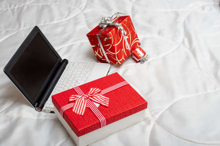 Online shopping concept. Red gift boxes and laptop with blank screen on white cloth background,...