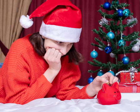 Saving money on Christmas gifts due to the pandemic crisis. Sad girl in a red christmas hat and...