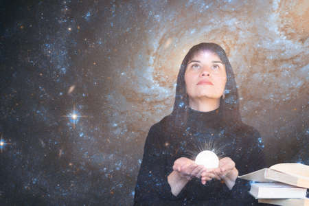 A girl with a star in her forehead holds a shining ball in her hands and looks up at the starry sky....