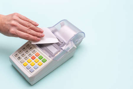 Close-up of a woman's hand tearing a check from an old cash register on a blue background, top view,...
