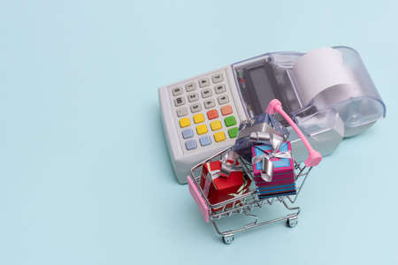 Online shopping concept. Close-up of a cash register next to a cart with wrapped boxes of gifts on a...