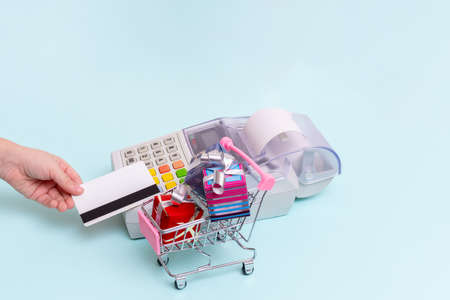 Close-up of a woman's hand holding a bank card over a cash register terminal for paying for...