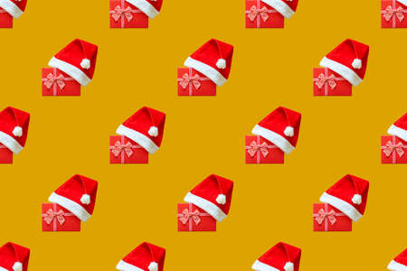 Seamless pattern with Christmas Santa Claus hat worn over a red gift against the trendy 2021 Fortuna Gold background, top view. Can be used as decorative elements for Christmas and New Yearの写真素材