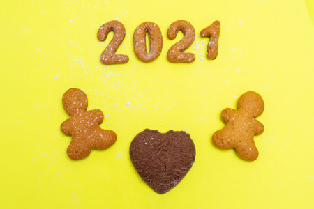 Love, family 2021 concept. Homemade cookies in the form of the numbers 2021, two gingerbread men and a heart of chocolate chip cookies between them on a yellow background, flat lay, copy spaceの写真素材