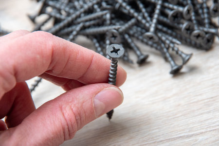 Hand holds a gray screw for screwing to a wooden background close-up, top view, copy space. Hardware, fasteners and materials for construction and repairの写真素材