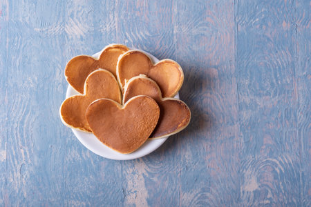 Homemade heart shaped pancake on a white plate on a blue wooden table, copy space, top view....