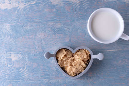 Healthy breakfast. Oatmeal in a heart shaped bowl, a spoon and a white cup of milk on a blue wooden table, copy space, top view. Healthy food conceptの写真素材