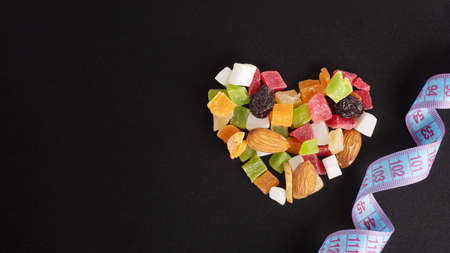 Diet food concept for Valentines Day. Slimming concept. Heart shaped dried fruits and nuts and measuring tape isolated on black background, copy space, close-upの写真素材