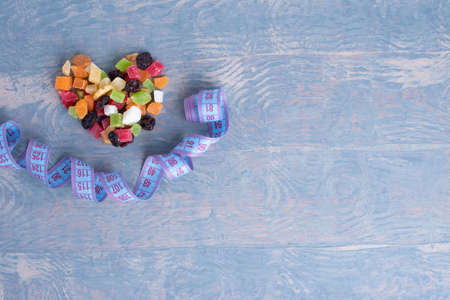 Weight control concept. Diet food concept. Dried fruits and nuts in the shape of a heart and a measuring tape looks like a smile on a blue wooden background, top view, copy spaceの写真素材