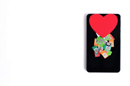 A pile of assorted used mobile SIM cards and a red paper heart on a cell phone on a white...