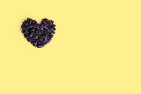 Roasted heart shaped sunflower seeds on trendy yellow background, copy space, top view.