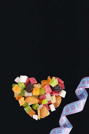 Diet food concept for Valentines Day. Slimming concept. Heart shaped dried fruits and nuts and measuring tape isolated on black background, copy space, vertical frameの写真素材