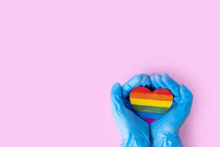 Two hands in protective blue gloves hold a rainbow paper heart on a pink background, copy space. Safe Valentines Day 2021 concept. LGBTQL conceptの写真素材