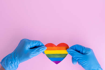 Two hands in protective blue gloves hold a rainbow paper heart on a pink background, copy space. Safe Valentines Day 2021 concept. LGBTQL conceptの写真素材