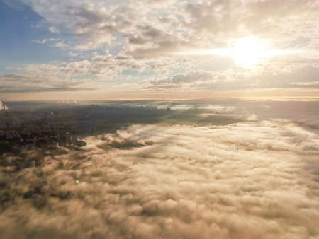 Travel concept. A beautiful view from the plane to the sun, multi-colored volumetric fluffy clouds, city skyscrapers below, top view. Beautiful natural sky backgroundの写真素材