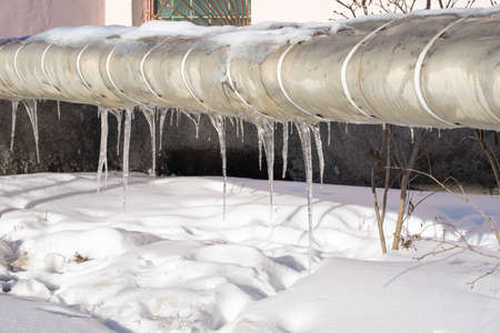 Very beautiful transparent icicles hanging from a snow-covered pipe. Spring melting snow. Icicles falling danger conceptの写真素材