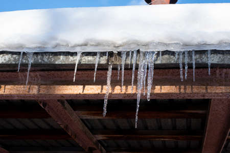 Long icicles hang from the snow-covered roof. Icicles falling danger concept.の写真素材