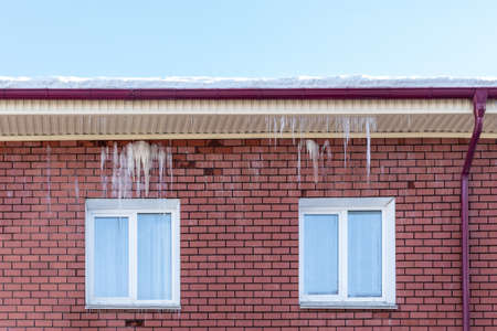 Transparent icicles hang from the snow-covered roof of a brick house. Spring melting snow. Icicles...