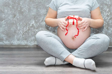 Close-up of a young pregnant woman holding a small white gift. Baby gift, birthday, mothers day,...
