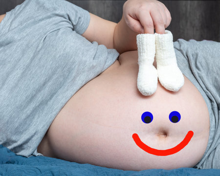 Just for fun. A pregnant woman holding baby knitted little socks in her hands and a drawn happy...