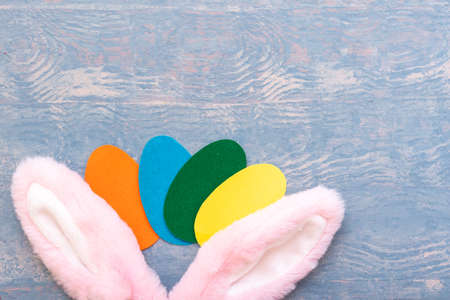 Happy Easter concept. Multicolored paper Easter eggs and pink bunny ears on a wooden blue backgroundの写真素材