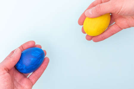 Happy Easter concept. Two hands give each other painted Easter eggs on a blue background, close-up, copy spaceの写真素材