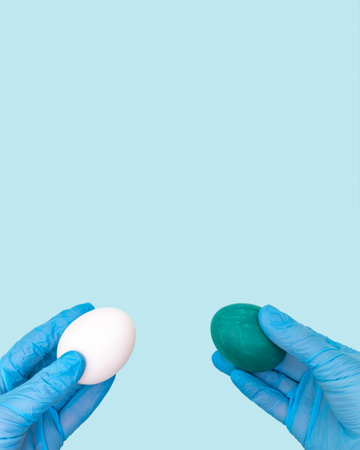 Happy and safe Easter concept. Two hands in protective medical gloves hold Easter eggs on a blue backgroundの写真素材