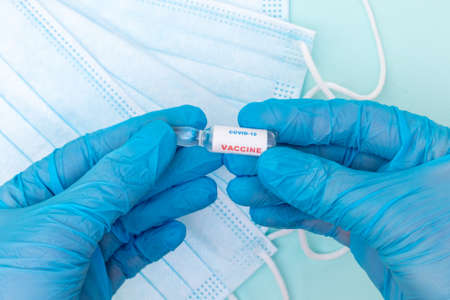 Closeup of a doctor hand in blue medical gloves holding an ampoule with a vaccine against coronavirus infectionの写真素材