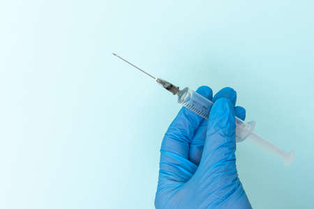 Close-up of a doctors hand in blue medical gloves holding a syringe with a medicine on a blue backgroundの写真素材