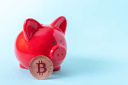 Bitcoin coin and red piggy bank on a blue background, close-up, copy space. Cryptocurrency saving concept.の写真素材