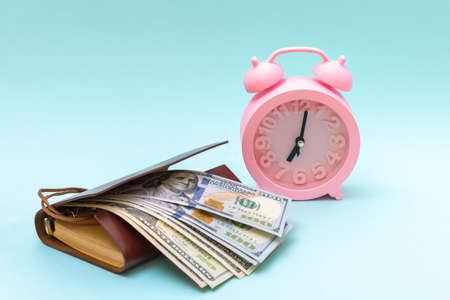 Pink alarm clock, dollars, notebook on a blue background, copy space. Business concept. Shopping conceptの写真素材