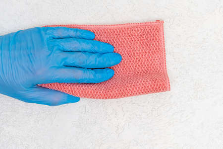 A hand in a blue rubber glove wipes the dust of a pink rag from a white plaster surface, copy space.の写真素材