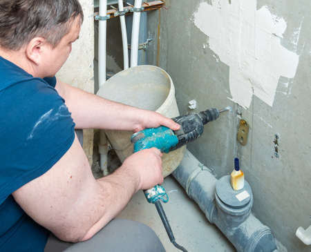 Repair, construction and DIY concept - close-up of a man with an electric drill making a hole in the wallの写真素材