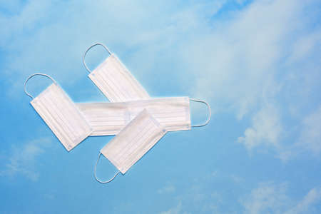 Airplane model made of protective masks on a bright blue sky with clouds. Safe travel by plane...
