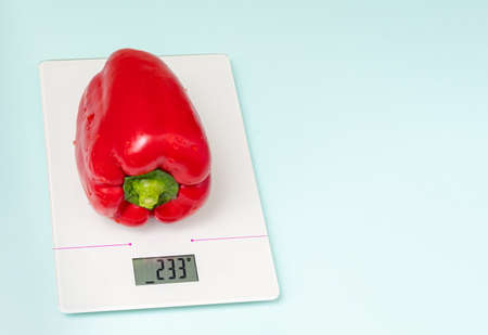 The concept of diet, proper nutrition, healthy eating. Fresh red bell peppers on kitchen scales isolated on blue background, copy space, close-upの写真素材