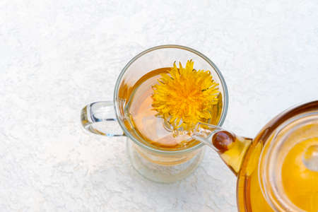 Pouring herbal dandelion tea into a transparent cup from a teapot on a white background, copy space, close-upの写真素材