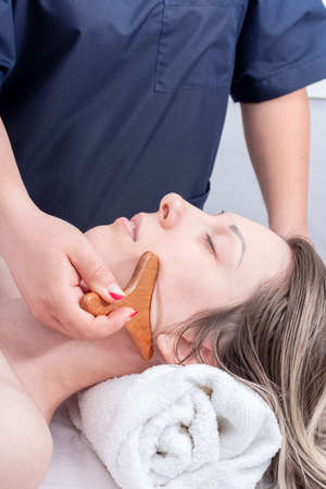 Massage the girls neck and face with a natural wooden massager, close-up. Face and neck care....