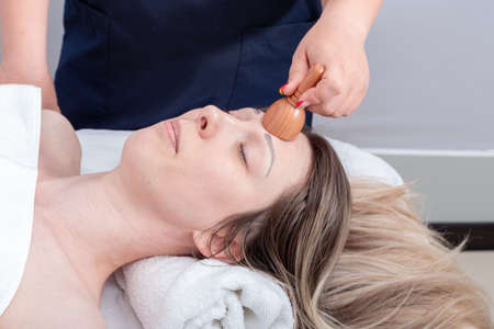 Hands of the masseur massaging the girls forehead with a natural wooden massager, close-up. Face...