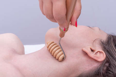 Madero therapy, anti-aging relaxing massage - Hands massaging the girls neck using a natural wooden massager. Face lifting massage, correction and removal of mimic wrinklesの写真素材
