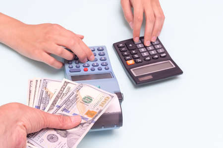 A hand giving cash for a purchase, a hand pressing buttons on a cash register, and calculating the cost on a calculator.の写真素材