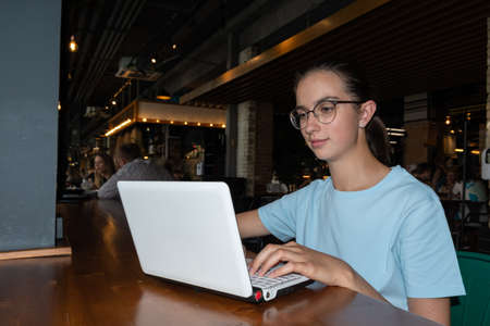 Beautiful girl student using a laptop, typing a message, searching the Internet sitting at a table in a loft cafeの写真素材