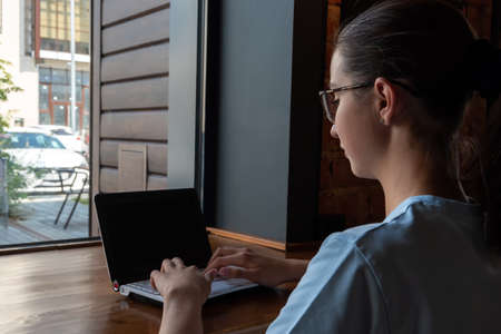 Beautiful girl student using a laptop, typing a message, searching the Internet sitting at a table in a loft cafeの写真素材