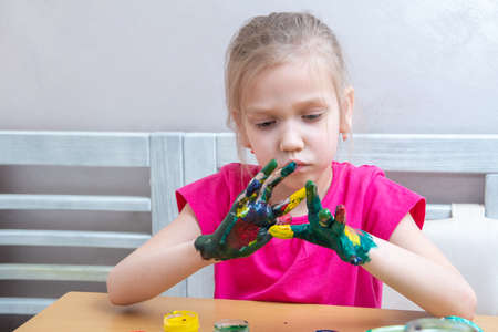 Little girl with colorful painted hands. A concentrated girl smears paints on her hands and looks at the result.の写真素材